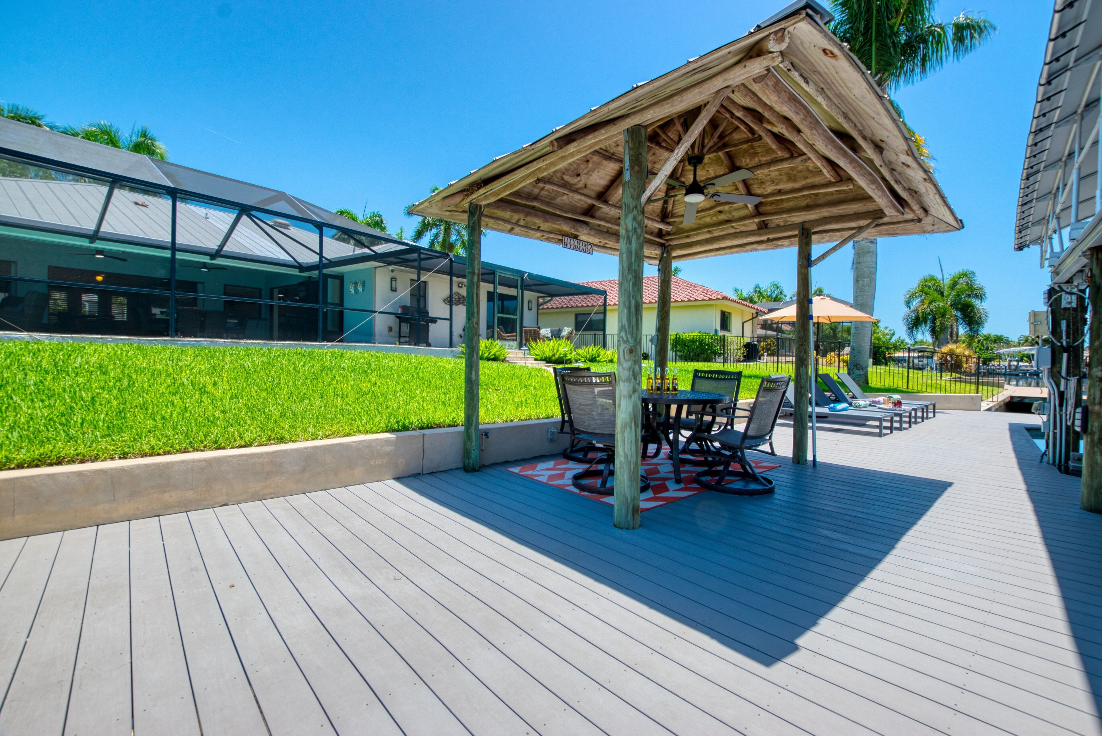 Un espace extérieur abrité, doté d’une table et de chaises, d’une pergola en bois et offrant une vue sur un bâtiment moderne aux murs de verre.