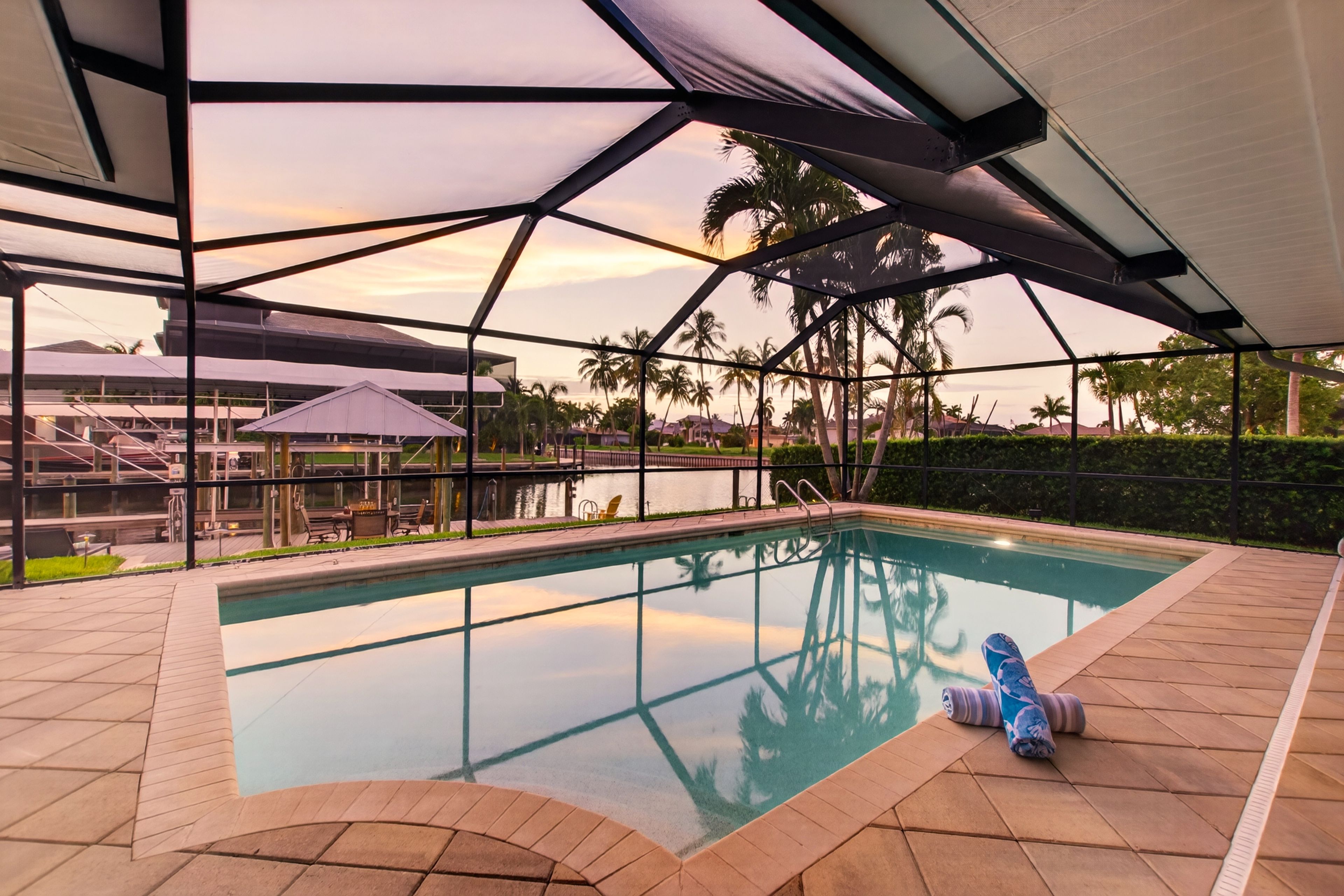 An outdoor swimming pool with a view of palm trees and a sunset.
