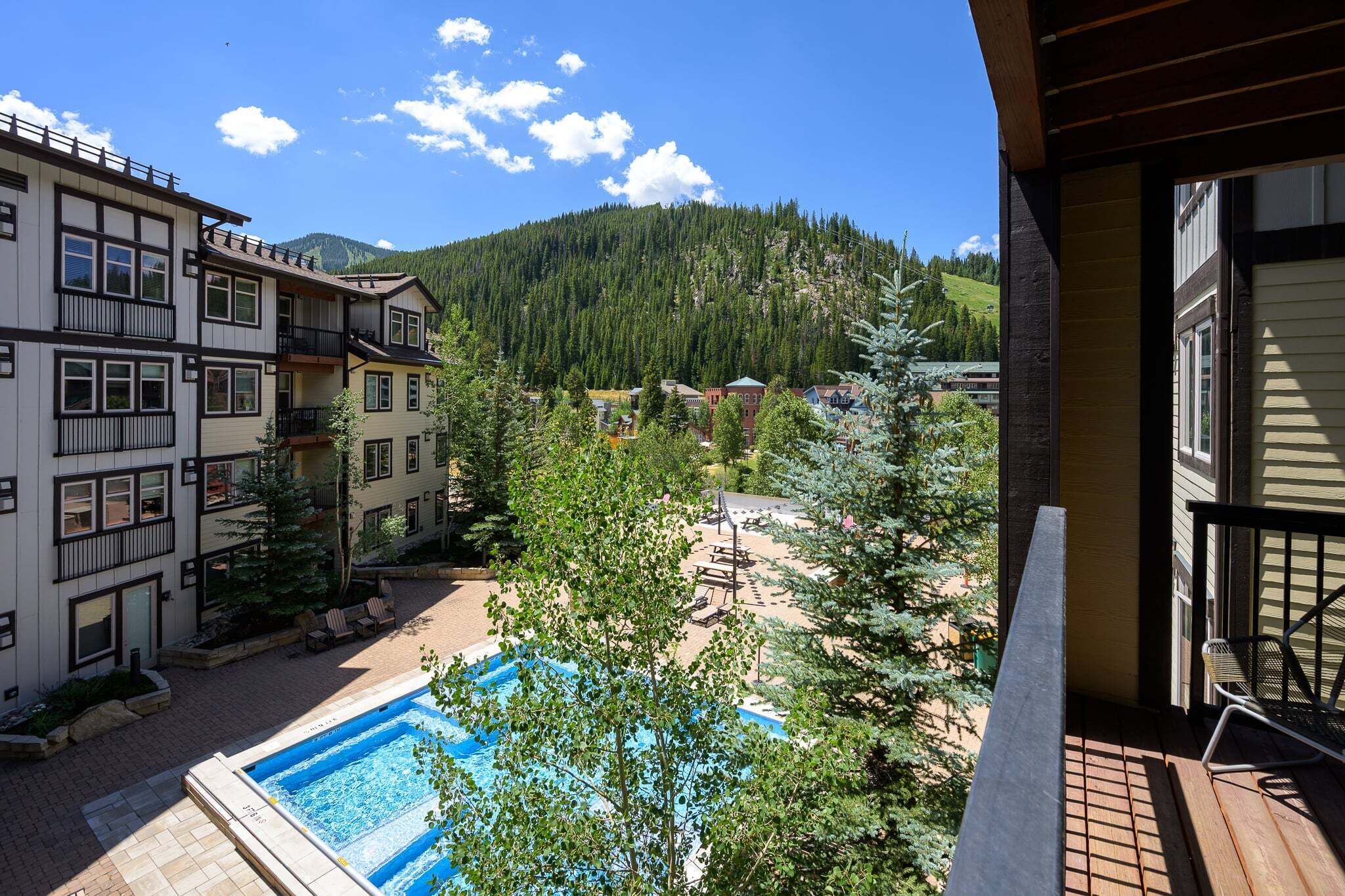 Un hotel con piscina, mobiliario exterior y vistas a una montaña boscosa.