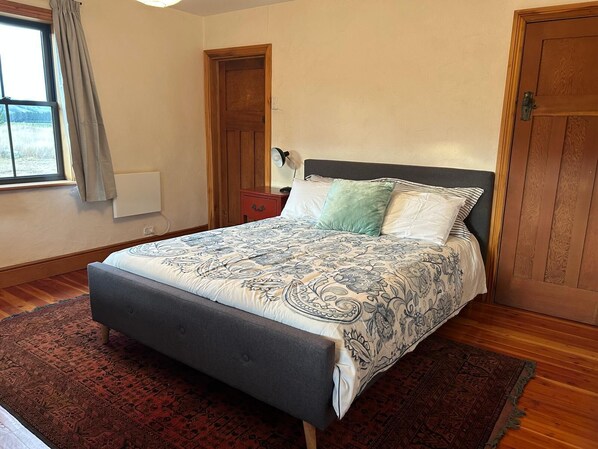 A bedroom with a bed, a nightstand, a lamp, a window with curtains, and a door.