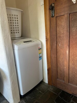 Ein Waschraum mit einer weißen Waschmaschine, einem weißen Wäschekorb und einer Holztür.