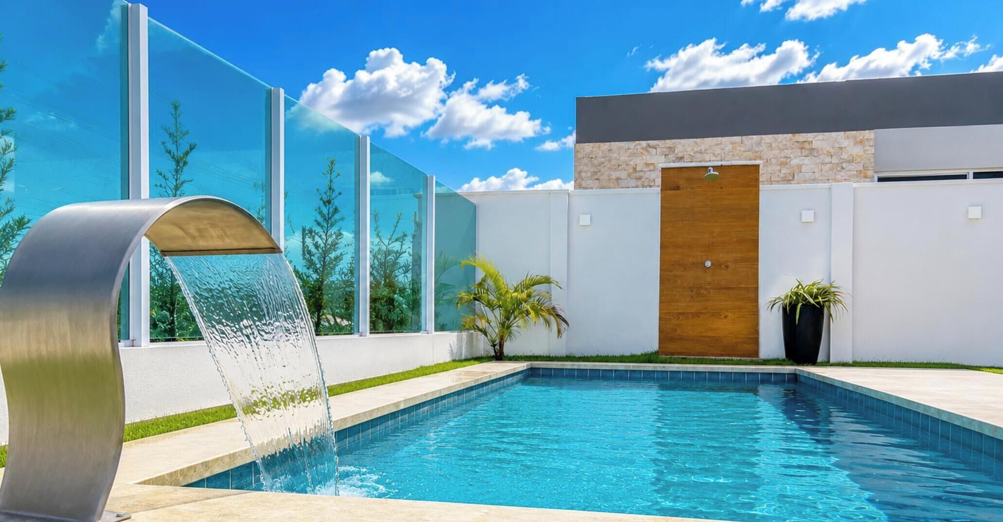 A modern outdoor swimming pool with a water feature, surrounded by a white wall and a stone facade.