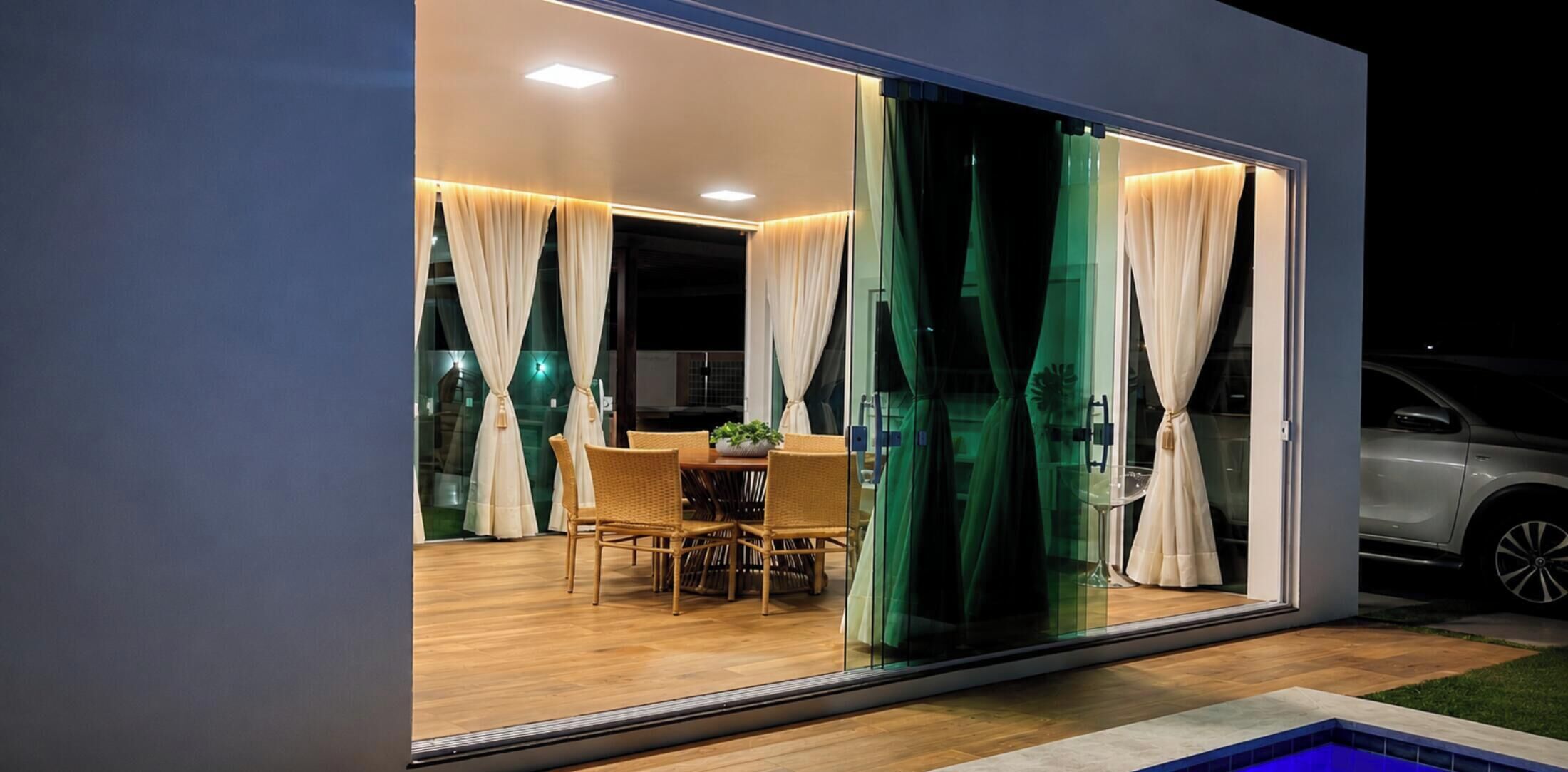 A modern house with a glass sliding door leading to an outdoor dining area with wicker furniture.