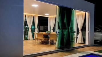A modern house with a glass sliding door leading to an outdoor dining area with wicker furniture.