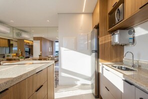 Cozinha moderna com ilha central, eletrodomésticos embutidos e vista para a sala de estar.