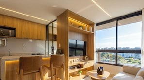 Cozinha moderna com armários de madeira, TV integrada e área de jantar com cadeiras.
