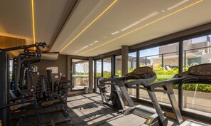 Academia moderna com equipamentos de exercício, grandes janelas e vista para o exterior.