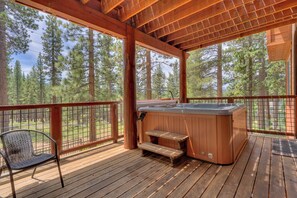 A wooden deck with a hot tub, a bench, and a chair.