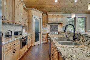 A kitchen with wooden cabinets, a granite countertop, stainless steel appliances, and a large window. - Game Room, Pool Table, Foosball, Arcade, Fireplace, Chef's Kitchen, Hot Tub, Sauna: Big Bear Lodge (South Lake Tahoe)