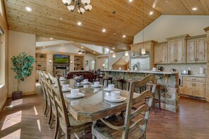A spacious kitchen with wooden cabinets, a dining area with a large table set for six, and a stone fireplace.