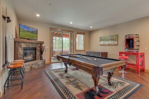 A pool table in a room with a stone fireplace, a television, and a painting on the wall.