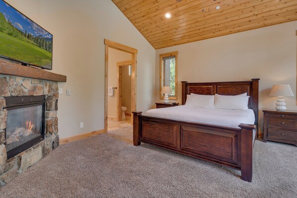 A bedroom with a stone fireplace, a wooden bed, and a view of a mountain landscape.