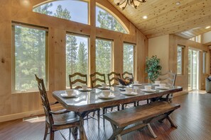 A dining area with a long wooden table set for six, surrounded by wooden chairs, large windows, and a ceiling with wooden beams. - Game Room, Pool Table, Foosball, Arcade, Fireplace, Chef's Kitchen, Hot Tub, Sauna: Big Bear Lodge (South Lake Tahoe)