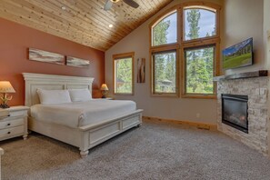 A bedroom with a large bed, a fireplace, and multiple windows.