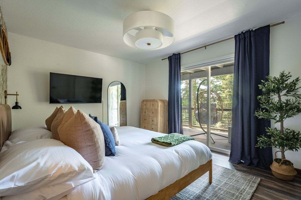 Een slaapkamer met een bed, een televisie aan de muur, een houten kast en een kamerplant.