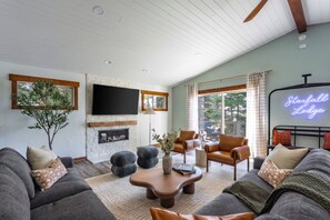 A spacious living room with a fireplace, comfortable seating, and a large window overlooking a deck. - Karaoke, Pool Table, Arcade, Outdoor Games, Bubble Dome, Grill, Spa: Starfall Lodge (Tahoe Vista)