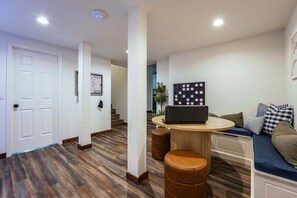 A modern interior with a wooden floor, a round table with a laptop, a sofa with patterned cushions, and a white door.