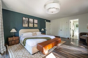 A bedroom with a bed, bedside tables, a bench, and a door leading to another room.