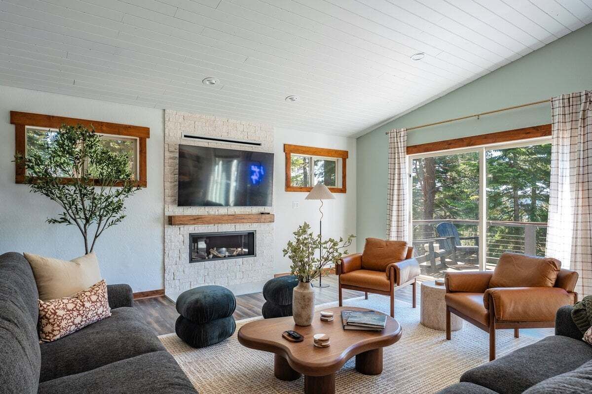 A modern living room with a fireplace, comfortable seating, and large windows.