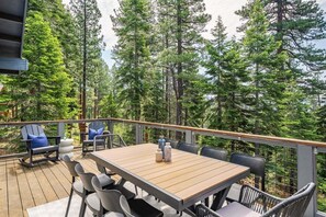 Una terraza al aire libre con una mesa y sillas de madera, rodeada de árboles altos.