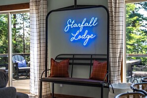 Ein Neon-Schild mit der Aufschrift 'Starfall Lodge' über einer Bank mit zwei Kissen.