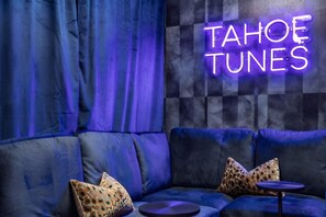 Una habitación con un letrero de neón que dice 'TAHOE TUNES' en la pared, un sofá azul con cojines de estampado de leopardo y una pequeña mesa redonda.