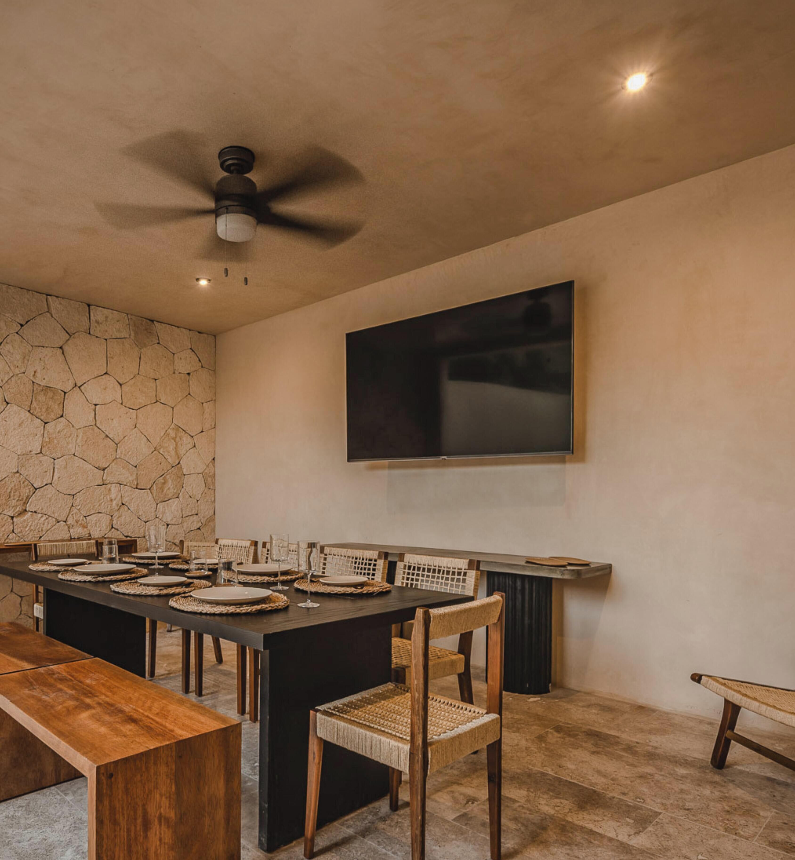 Un coin repas agrémenté d’un mur en pierre, d’un ventilateur de plafond et d’un téléviseur à écran plat fixé au mur.