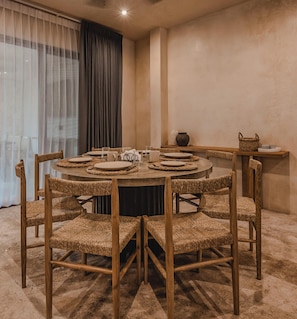 Un comedor con una mesa redonda, sillas tejidas y un ventilador de techo.
