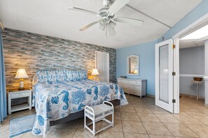 Ein Schlafzimmer mit einem Bett, zwei Nachttischlampen, einem Deckenventilator, einem Nachttisch, einer Kommode, einem Spiegel und einer Tür.