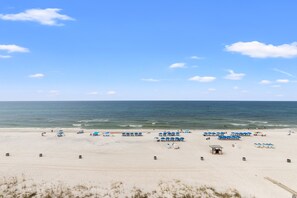Ein Strand mit Liegestühlen und Sonnenschirmen, einem Rettungsturm und dem Meer im Hintergrund.