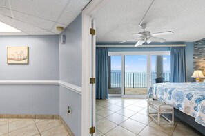 A hotel room with a large balcony, a ceiling fan, and a bed with a blue and white patterned bedspread. - Beachfront 2BR/2BA condo with pool views, balcony, free beach service. (Panama City Beach)