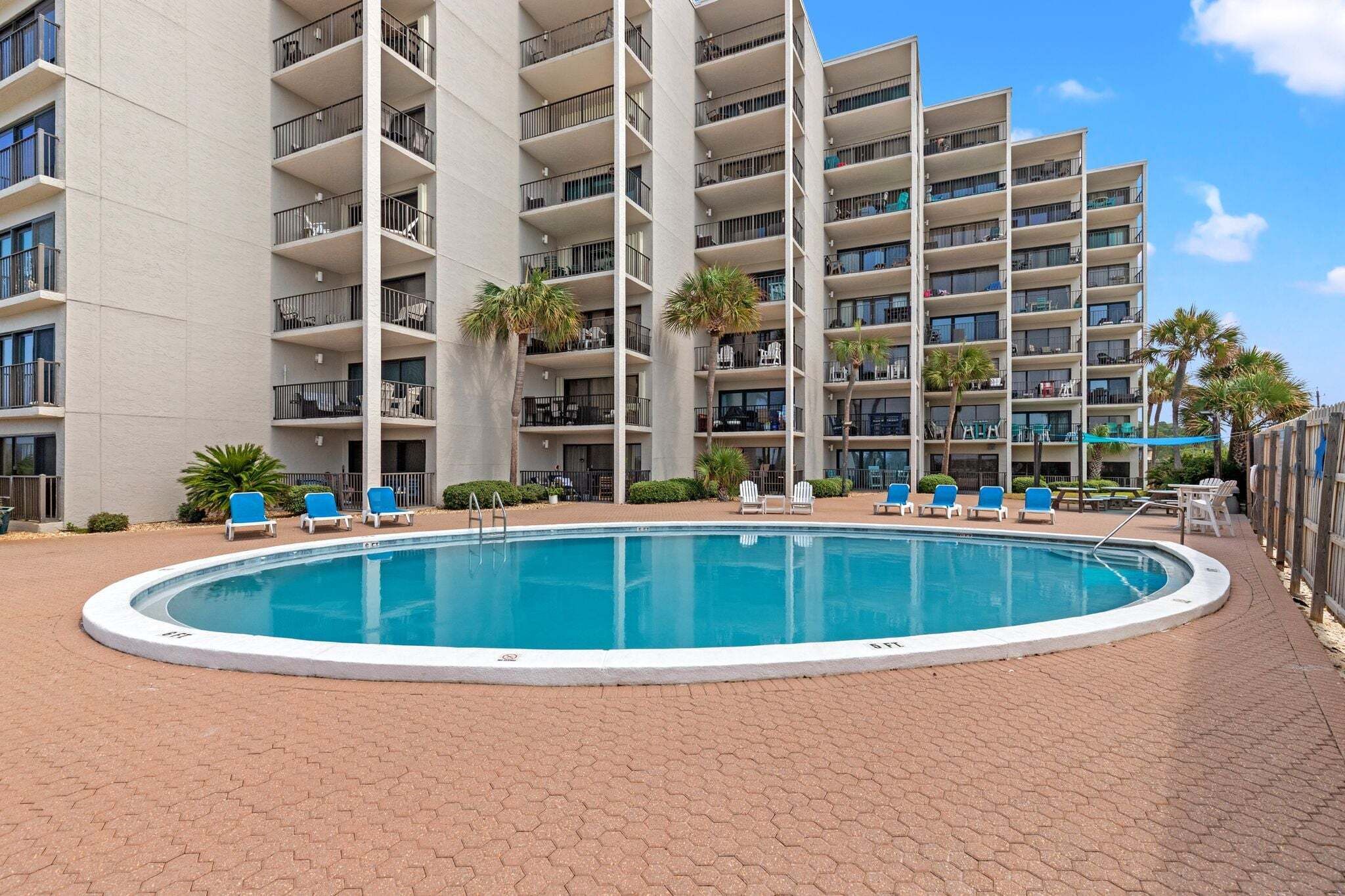 A multi-story hotel with a swimming pool surrounded by lounge chairs and palm trees.