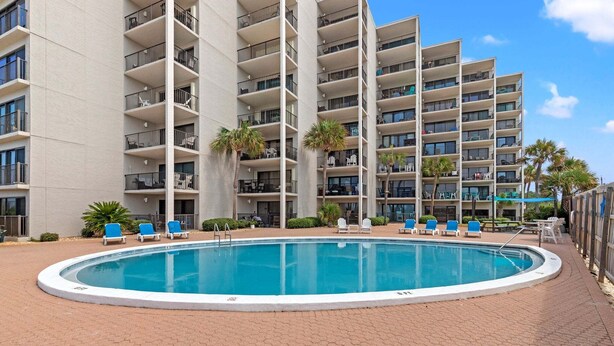 Et hotel med flere etager, med en swimmingpool omgivet af liggestole og palmer.