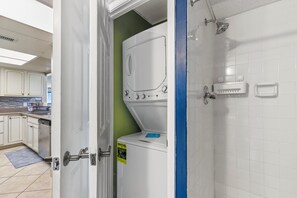 Ein Waschraum mit nebeneinander gestapelten Waschmaschine und Trockner, einer Dusche und einer gefliesten Wand.