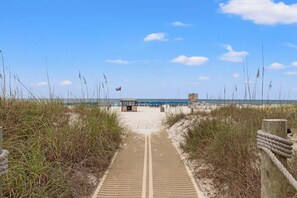 A beach pathway leading to a beach area with umbrellas and a lifeguard station. - Beachfront 2BR/2BA condo with pool views, balcony, free beach service. (Panama City Beach)