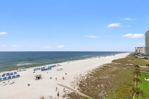 Ein Strand mit Sonnenschirmen, einem Rettungsturm und einer Promenade, die zum Meer führt.