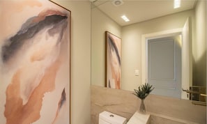 Een badkamer met een marmeren wastafel, een toilet en een grote spiegel die een deur en een schilderij weerspiegelt.