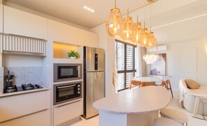 Een moderne keuken met een ingebouwde oven, magnetron en koelkast. Er is een rond kookeiland met zitplaatsen en een eettafel met stoelen.