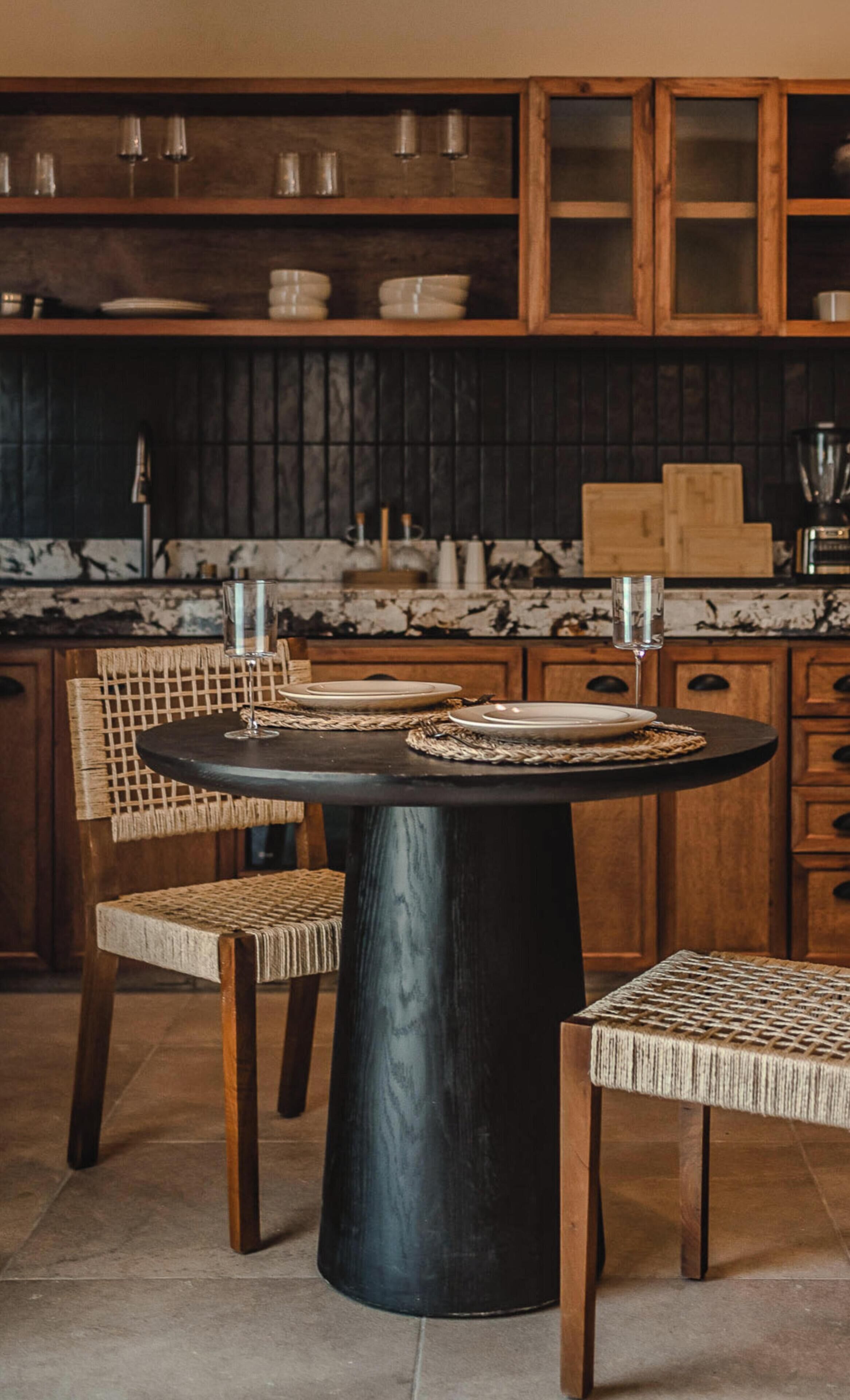 Un comedor con una mesa redonda, dos sillas y una cocina al fondo.