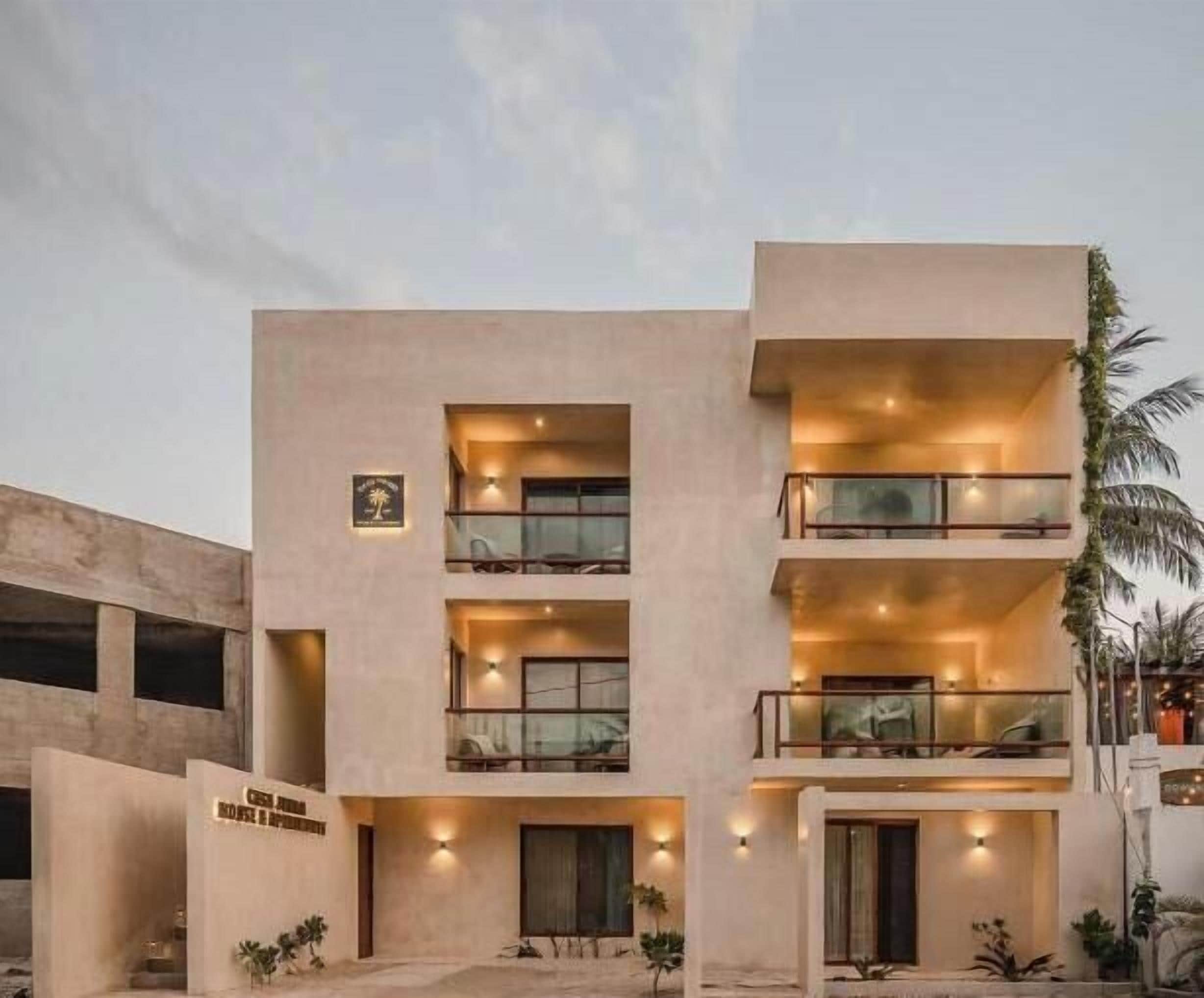 Un hotel de varios pisos con balcones, un letrero que indica un restaurante y una palmera en primer plano.