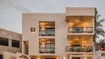 Un hotel de varios pisos con balcones, un letrero que indica un restaurante y una palmera en primer plano.