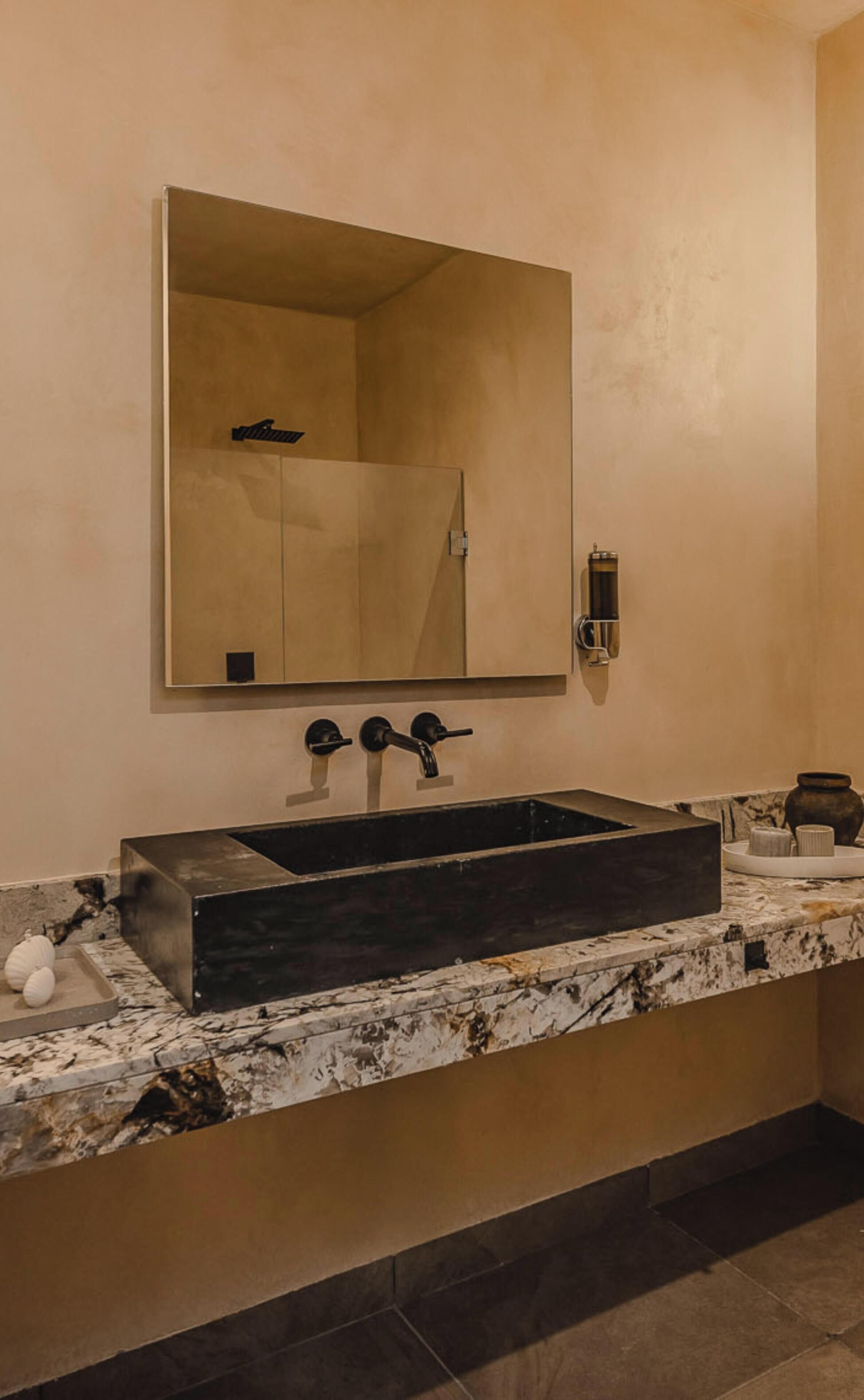 A bathroom with a rectangular sink, a large mirror, and a wall-mounted faucet.