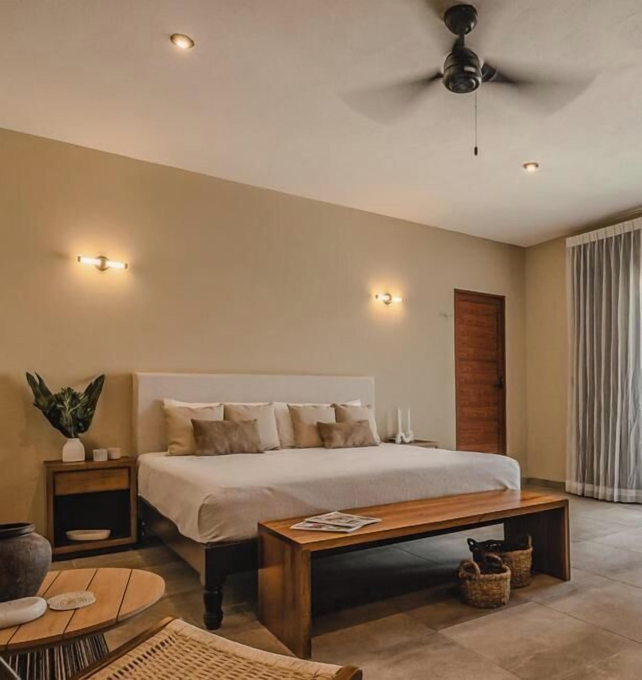 Un dormitorio moderno con una cama grande, mesitas de noche, ventilador de techo y vistas al exterior.