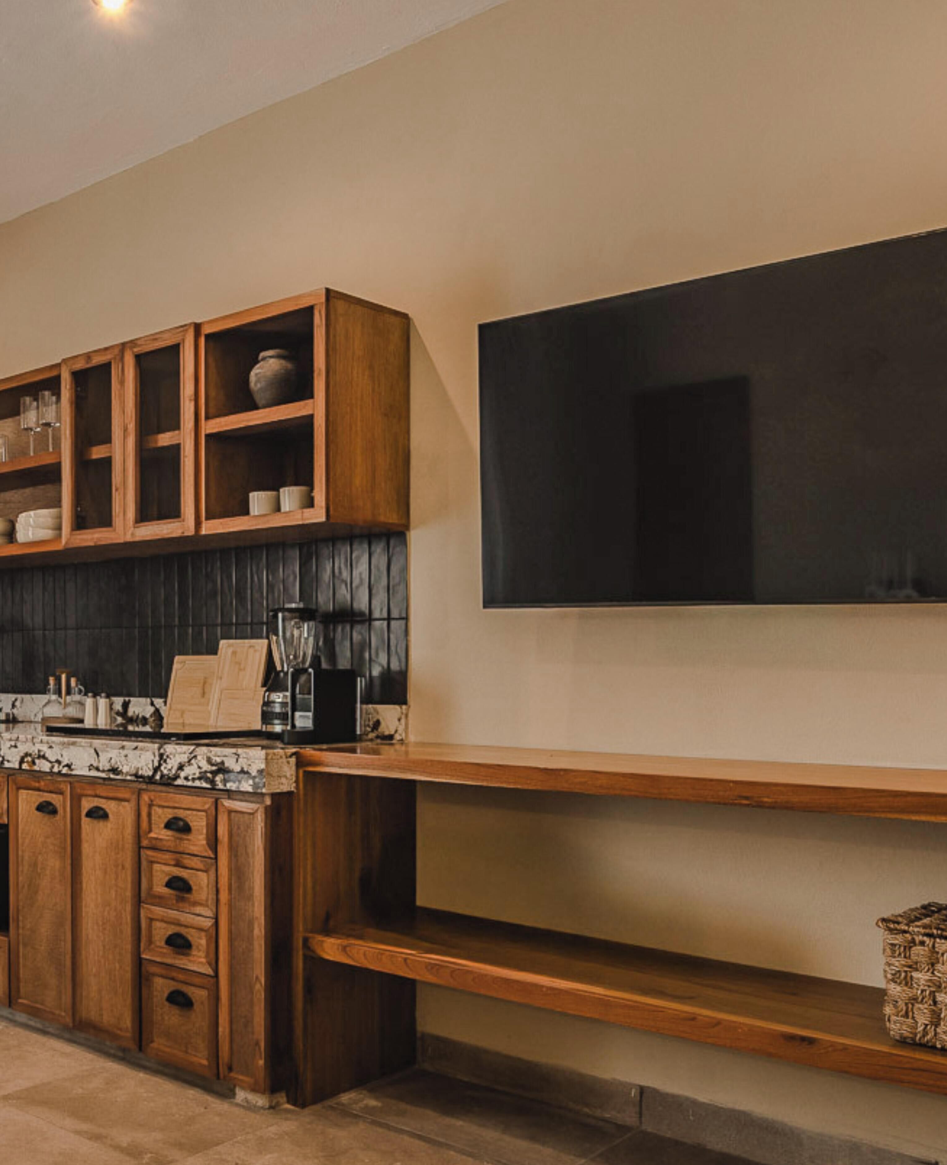 Une cuisine moderne avec des meubles en bois, un plan de travail noir et un grand téléviseur à écran plat fixé au mur.