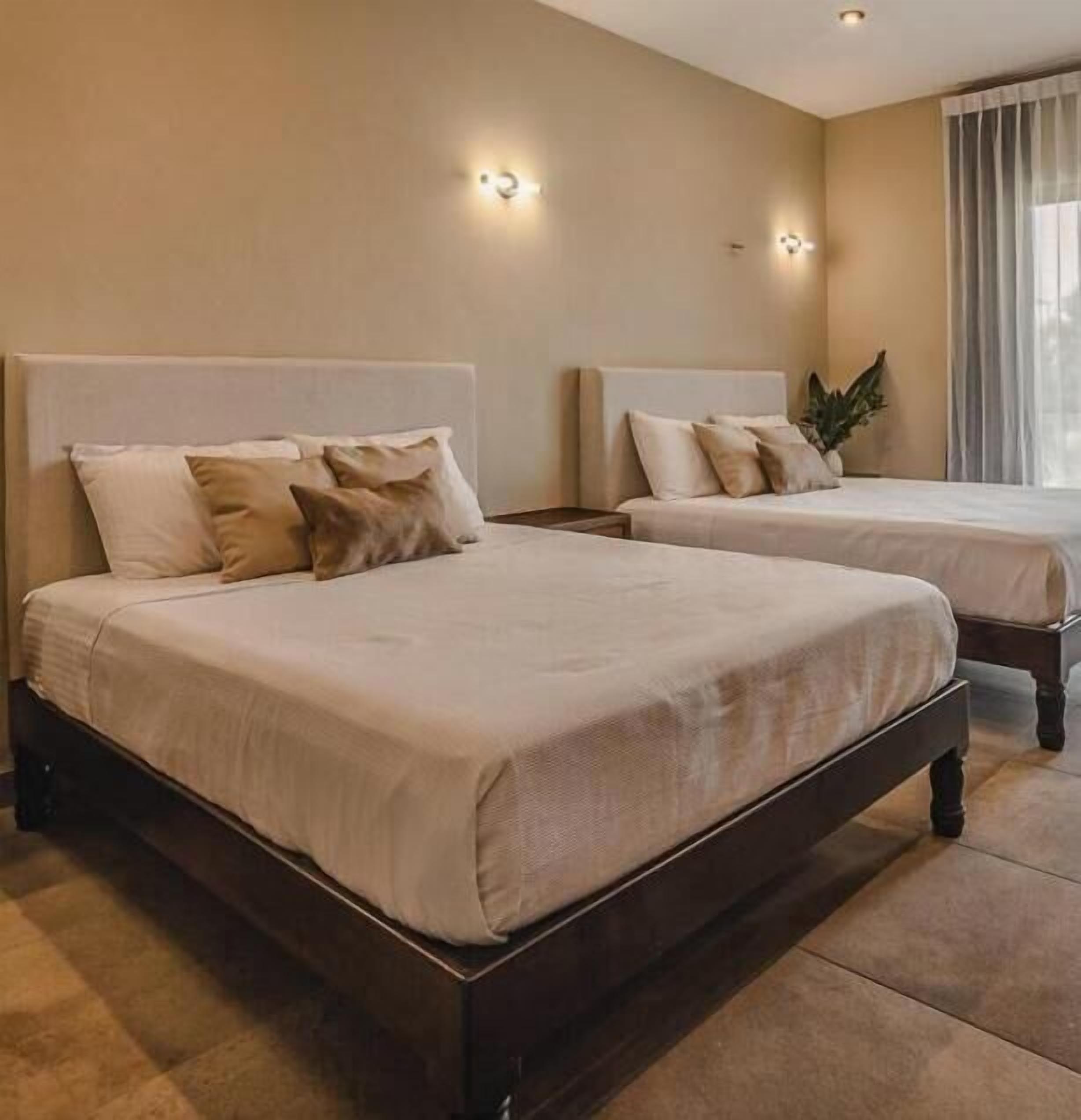 Une chambre d’hôtel avec deux lits, une grande fenêtre avec des rideaux et des lampes fixées au mur.