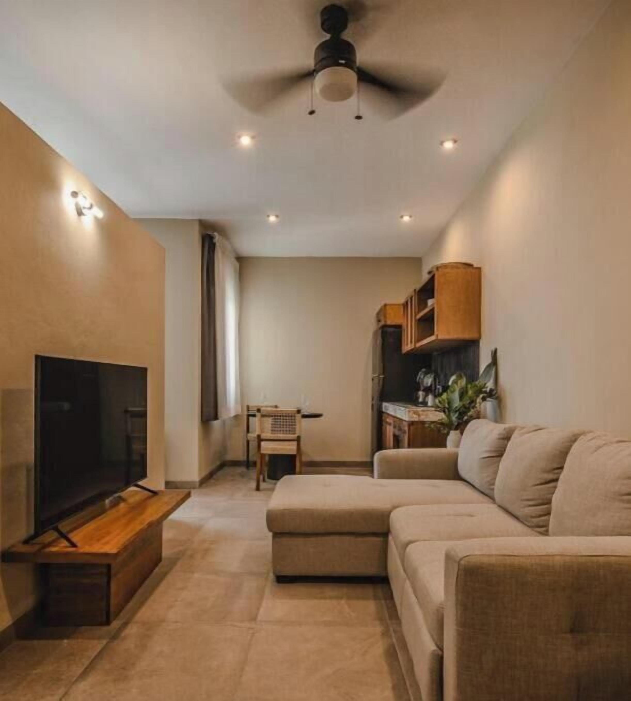 Un salon comprenant un canapé, un téléviseur, un ventilateur de plafond et un éclairage encastré.