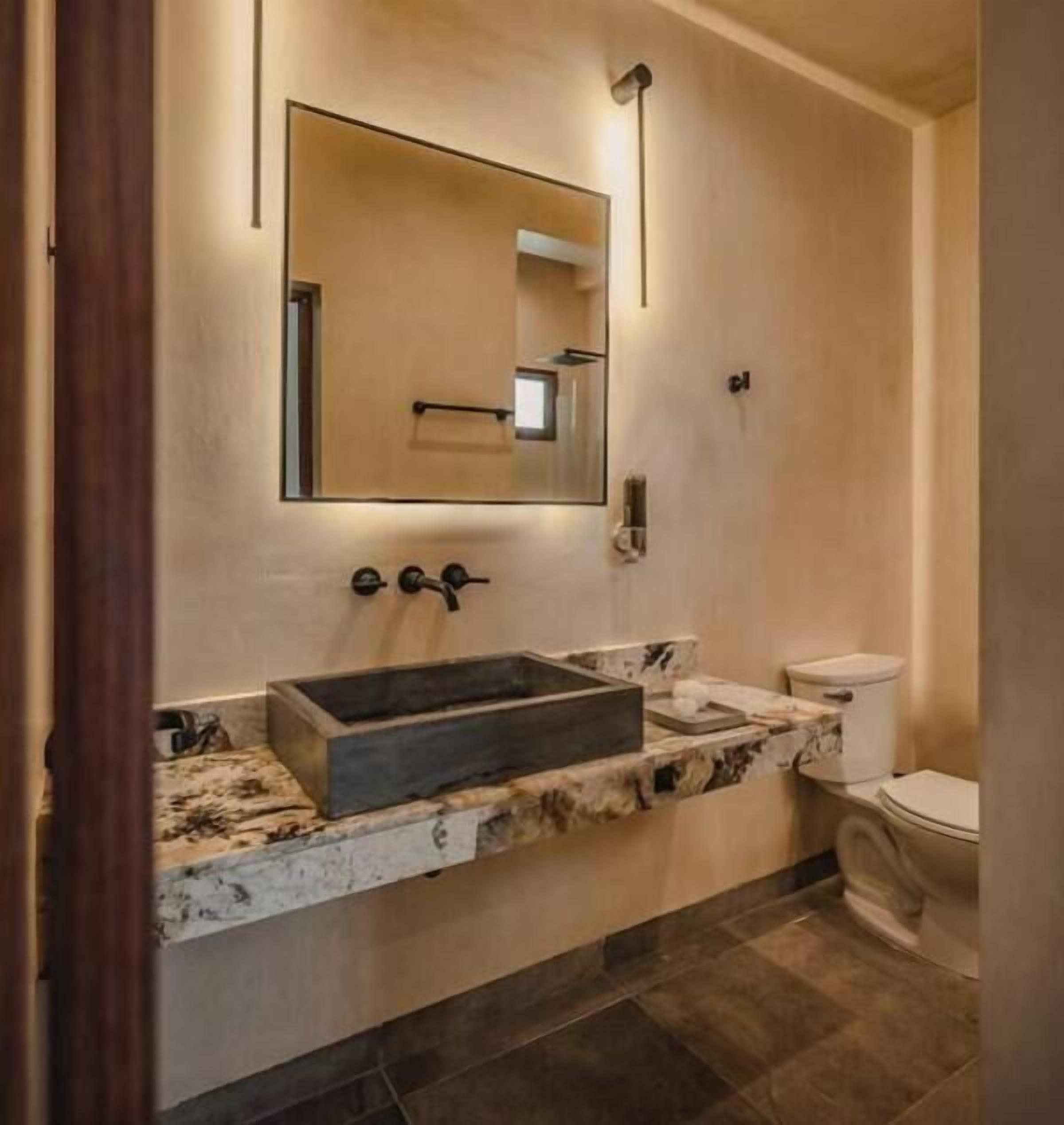 Un baño con un lavamanos rectangular, un inodoro y un espejo instalado en la pared.