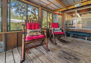 A wooden deck with two rocking chairs, one with a cushion and a pillow, and a bench. - Red Canoe Cabin on the water in National Forest (Salt Springs)