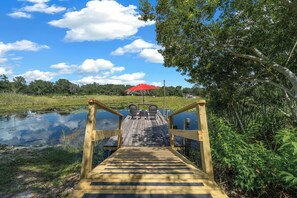 A wooden bridge leading to a red umbrella over a pond, surrounded by greenery. - Red Canoe Cabin on the water in National Forest (Salt Springs)