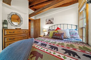 A bedroom with a wooden dresser, a bed with a colorful quilt, a mirror, and a bear-themed pillow. - Red Canoe Cabin on the water in National Forest (Salt Springs)